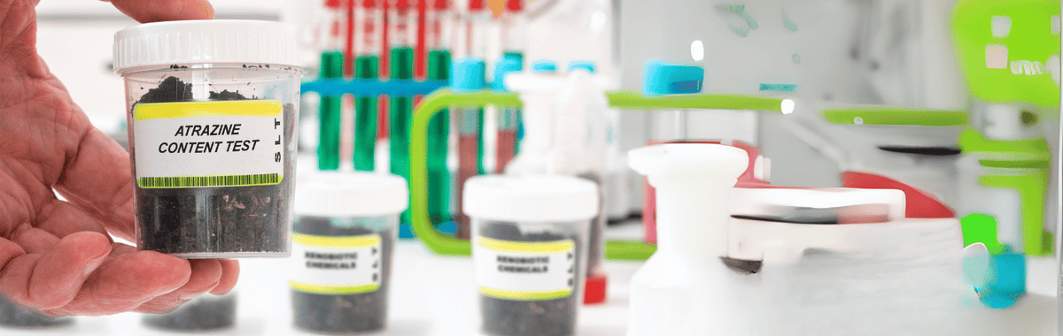Hand holding a water sample labeled atrazine content test in a lab
