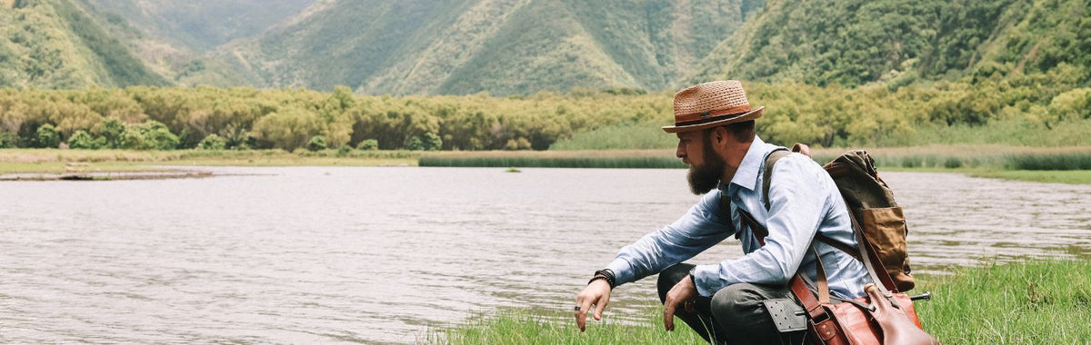 Man in a hat kneeling by a lake to gather plants