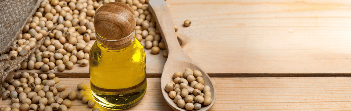Glass jar of soybean oil with soybeans and a wooden spoon