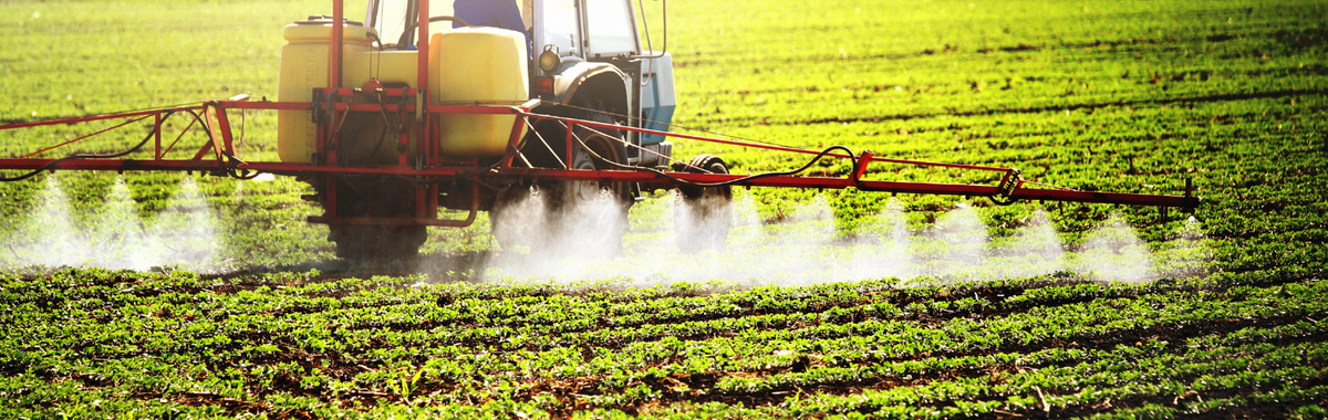Tractor spraying pesticide over a crop field