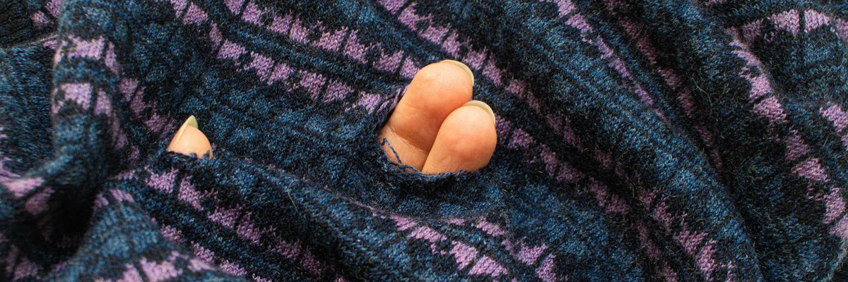 Fingers poking through moth holes in a knit sweater