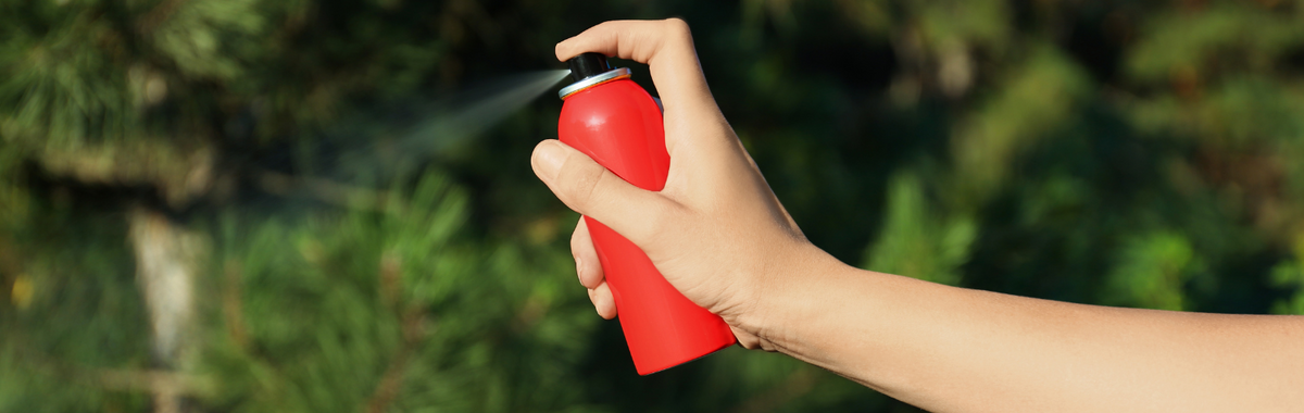 Hand spraying a red aerosol insecticide outdoors; permethrin kills many common bugs